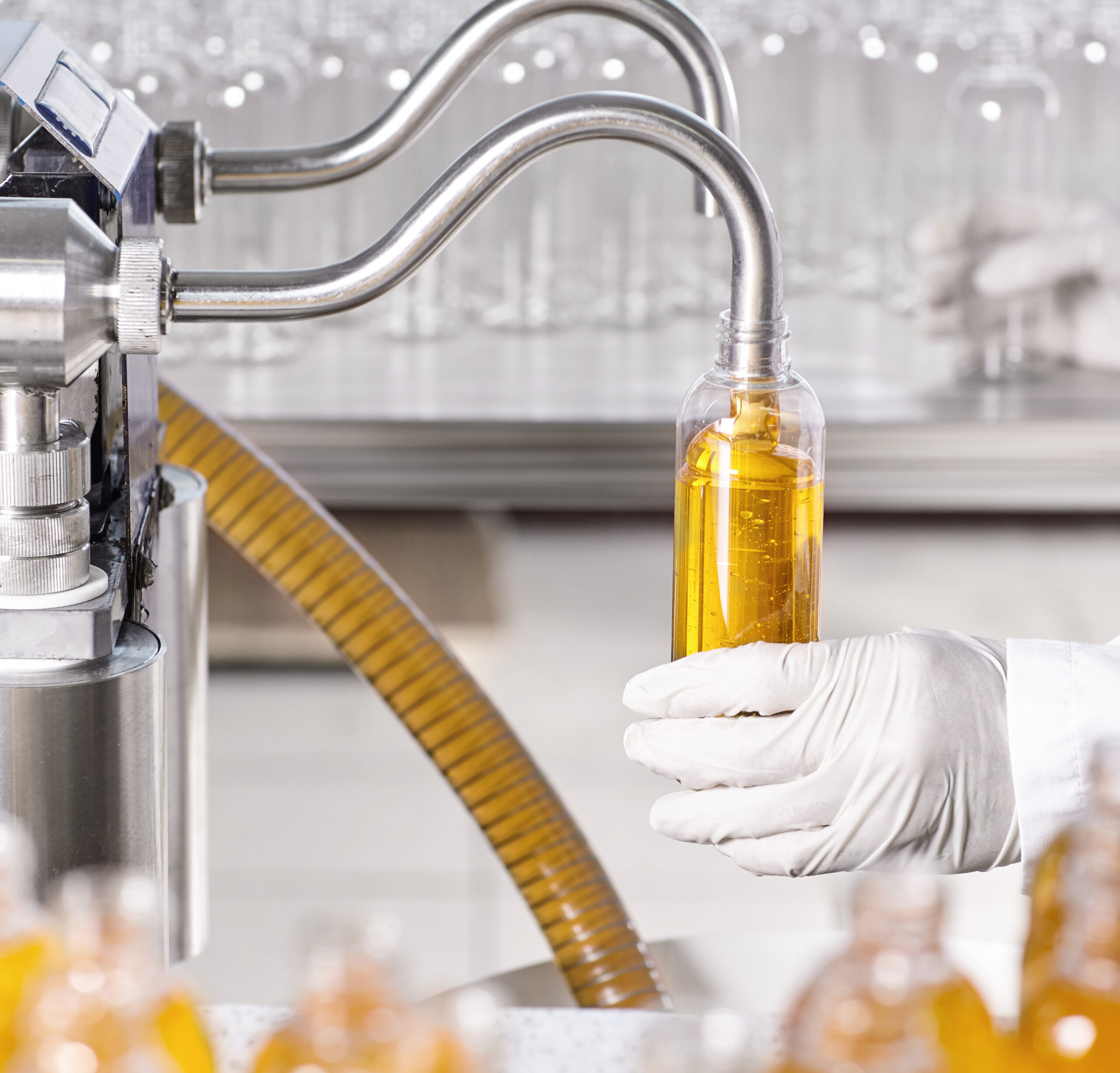 Medicine, healthcare, chemistry, pharmacy and cosmetology concept. Factory worker wearing white gown and gloves pouring thick yellow substance in transparent glass or plastic bottle at pruduction line