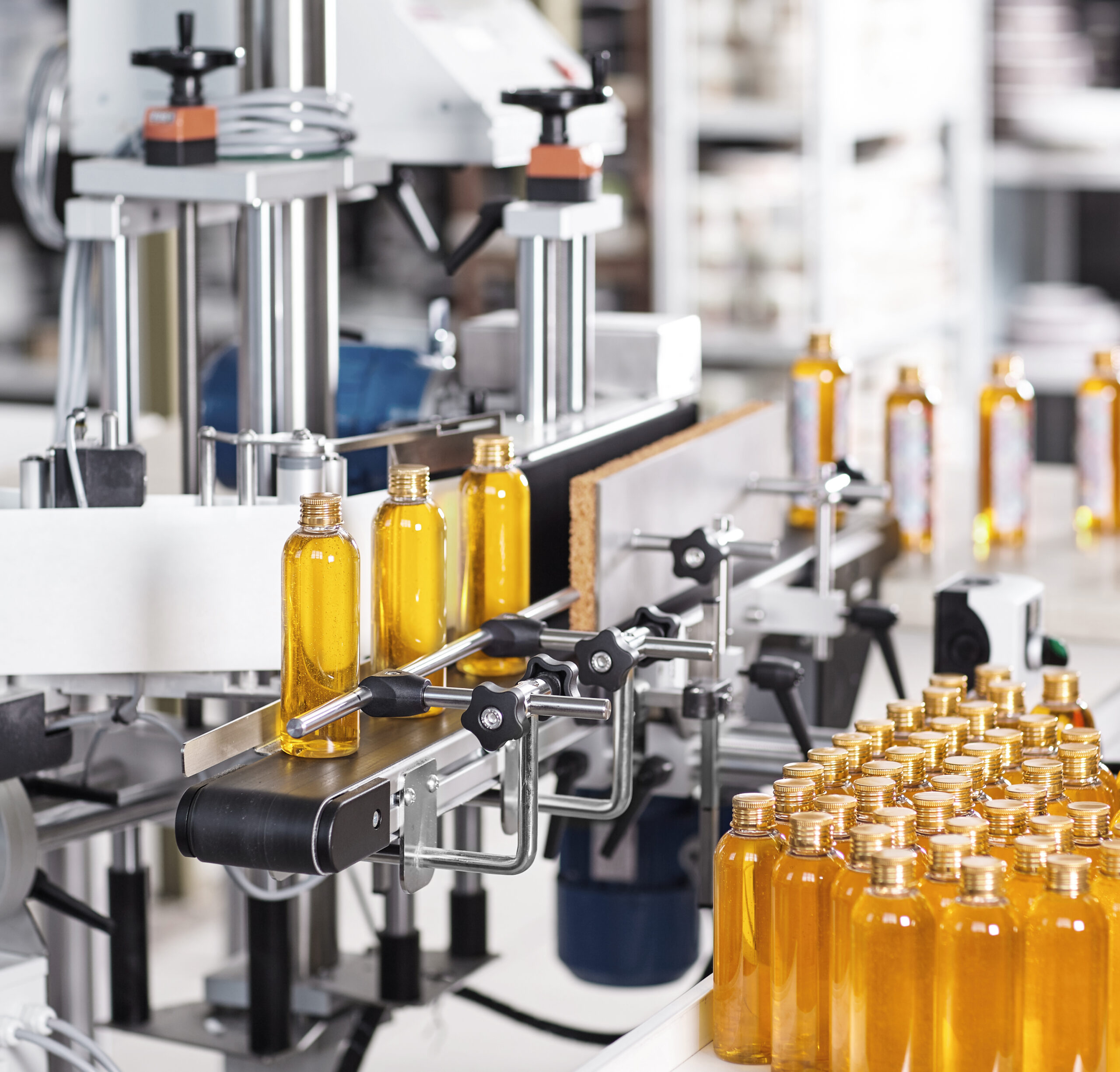 Horizontal shot of cosmetics or pharmacy plant with automated equipment. Transparent plastic bottles filled with yellow substance standing on desk and conveyor line, ready for transportation